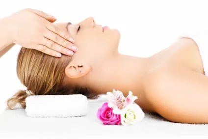 Massage du visage, tête posée sur une serviette roulée près de fleurs